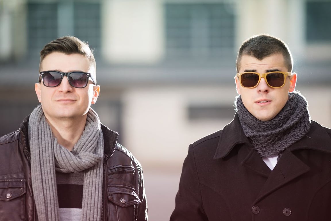 Two men in leather jacket, wool coat, scarves, and sunglasses