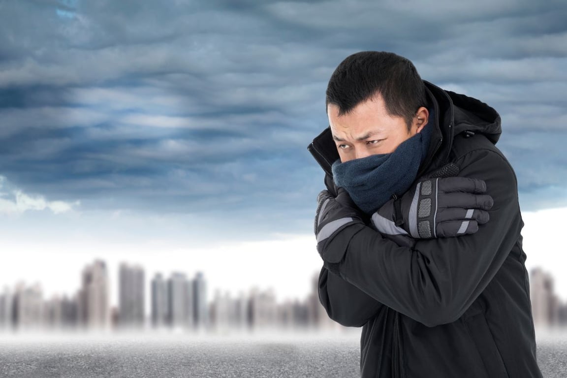 Man shivering in extreme cold wearing a black heavy jacket, gloves, and blue scarf over his mouth