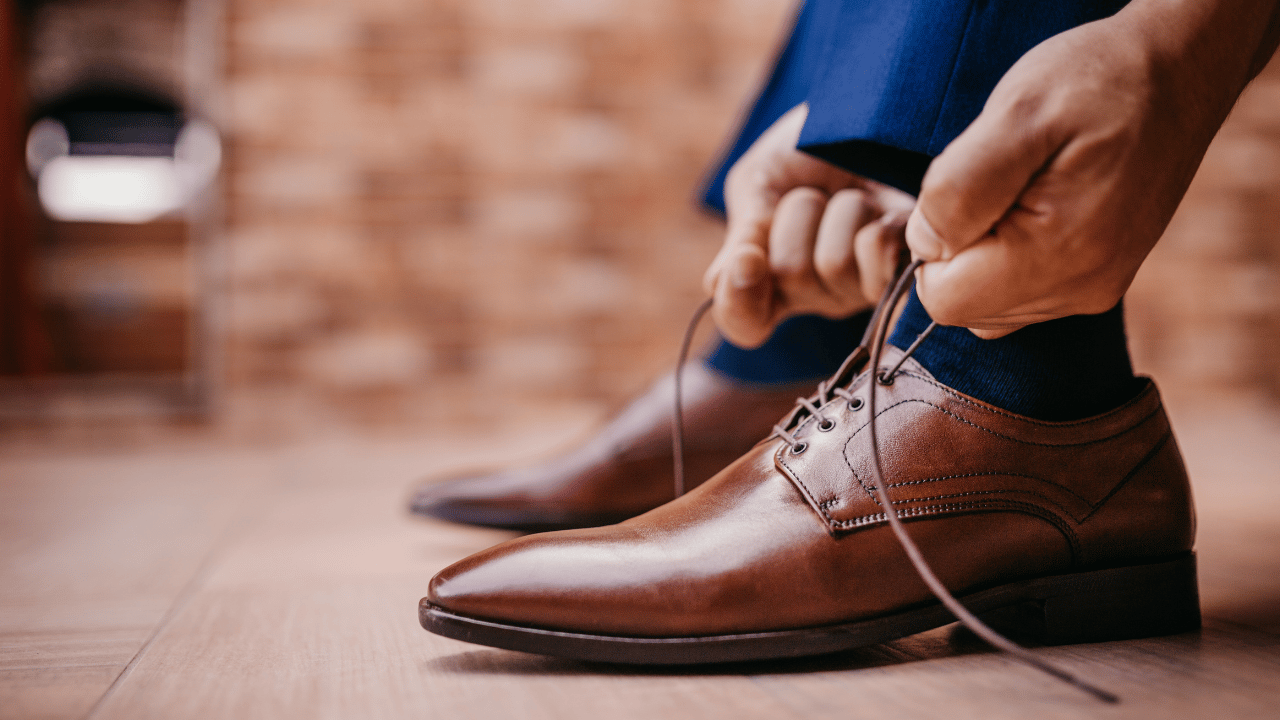 a man tying a light brown shoe on a navy suit